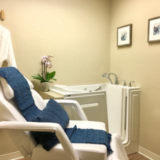 A calming spa room featuring a comfortable chair and a walk-in bathtub with minimalist decor.