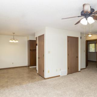 A spacious living area with carpeted flooring, ceiling fan, and multiple doors leading to other rooms.
