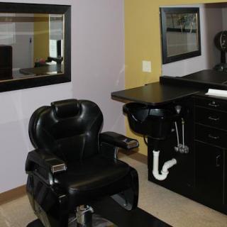 A barbershop interior featuring a barber chair, mirror, and sink setup.
