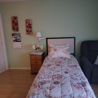 A cozy bedroom with a single bed featuring floral bedding, a nightstand with a lamp, and wall art.
