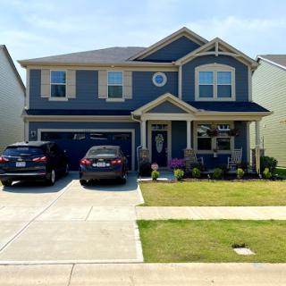 A charming two-story family home with a well-kept lawn and cars parked in the driveway.