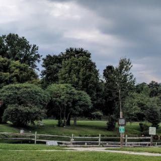 A serene park scene featuring lush greenery and a peaceful water body under a cloudy sky.