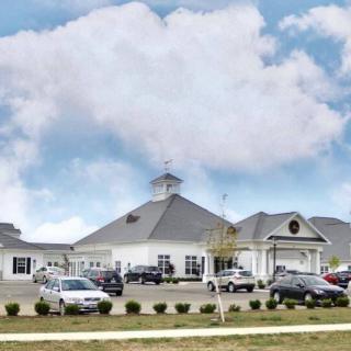 A large building with a parking lot in front, surrounded by cars under a cloudy sky.