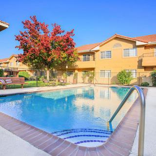 A residential complex featuring an outdoor swimming pool and landscaping under a clear blue sky.