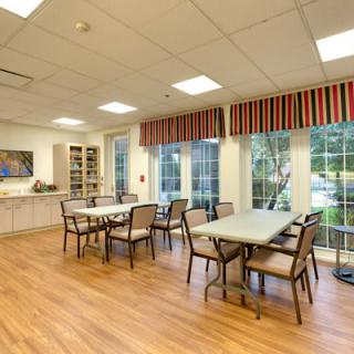 A well-lit dining area with tables and chairs, featuring large windows and a wooden floor.