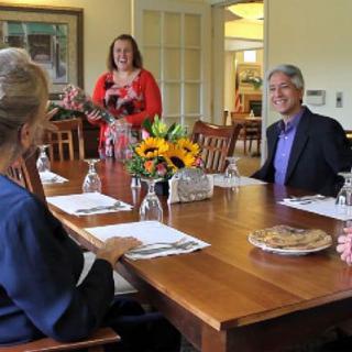 A group of people sitting around a dining table having a discussion with flowers as a centerpiece.