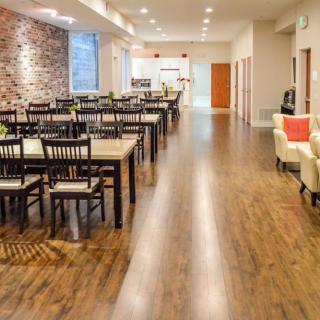 A modern restaurant dining area with wooden floors, tables and chairs, and a brick accent wall.