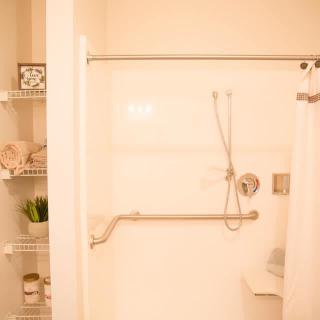 A well-organized bathroom featuring a walk-in shower with a grab bar and adjacent shelving.