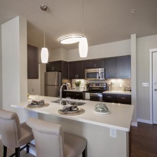 A modern kitchen with stainless steel appliances, pendant lighting, and a cozy breakfast bar with bar stools.