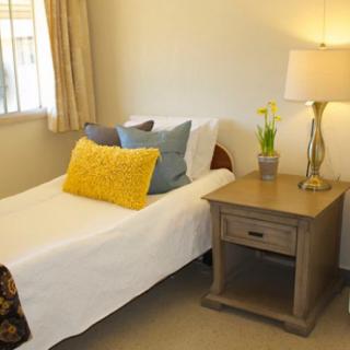 A cozy bedroom with a single bed, adorned with colorful pillows, next to a wooden nightstand and lamp.