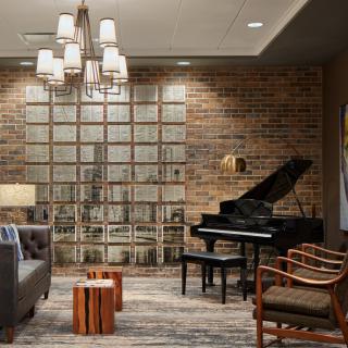 A stylish living room featuring a grand piano, modern furniture, and a brick accent wall.