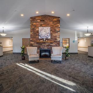 A cozy lobby interior with a central fireplace, flanked by two armchairs and decorative plants.