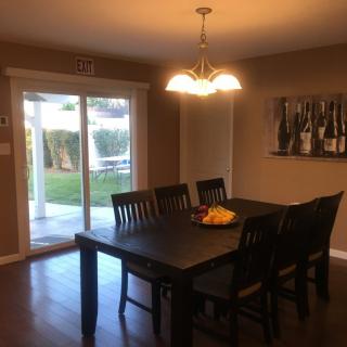 A cozy dining room with a dark wooden table and chairs, a chandelier above, and artwork on the wall.
