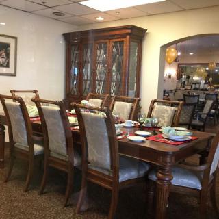 A formal dining room with a large wooden table surrounded by chairs, set for a meal.