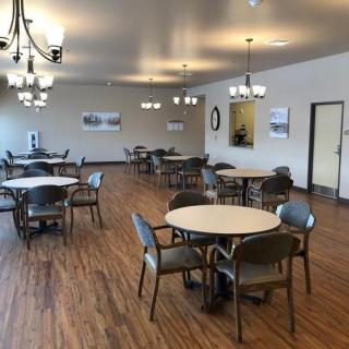 A spacious dining area with round tables and chairs, featuring chandeliers and wood flooring.