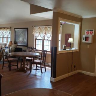 A cozy dining area with a round table and chairs, featuring large windows and a warm decor.