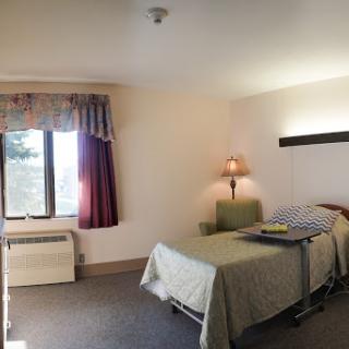 A simple, well-lit hotel room featuring a bed, window, and lamp.