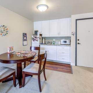 A compact dining and kitchen area with a wooden table, chairs, white cabinets, and essential appliances.