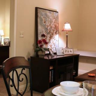 A cozy dining room featuring a wooden table set with white bowls, alongside a sideboard with a lamp and decorative items.