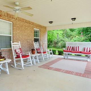 A cozy porch with white rocking chairs and a swing, decorated with red cushions, creating an inviting outdoor seating area.