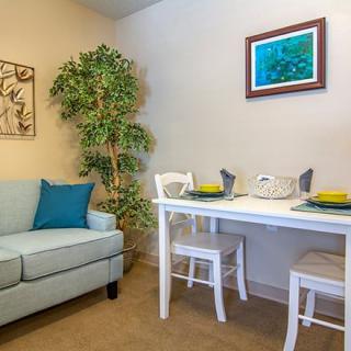 A cozy living room with a small dining area, featuring a sofa, table with chairs, and decorative wall art.