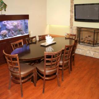 A modern dining room featuring an oval table with chairs, an aquarium, a fireplace, and a wall-mounted TV.
