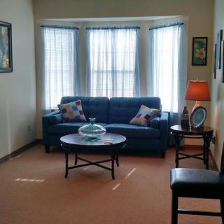 A cozy living room with a sofa, coffee table, and bright windows.