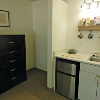 A compact kitchenette area with a mini fridge, sink, and cabinets alongside a tall dresser.