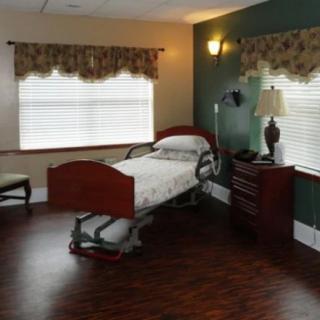 A well-furnished hospital room featuring a single bed, with elegant wooden flooring and a lamp on a nightstand beside the bed.