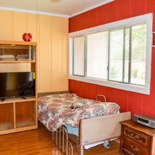 A cozy bedroom featuring a single bed, wooden flooring, and a shelving unit with a television.