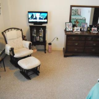 A cozy living room with a chair, ottoman, dresser, and television.