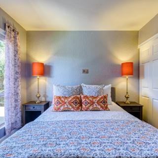 A cozy bedroom with a neatly made bed, flanked by two side tables and orange lamps.