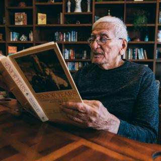 A senior man enjoys reading a book in a cozy library.