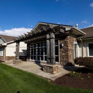 A beautifully designed modern home with a stone facade and a pergola, surrounded by lush landscaping.