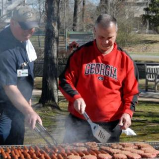 Two individuals grilling food outdoors in a park setting.