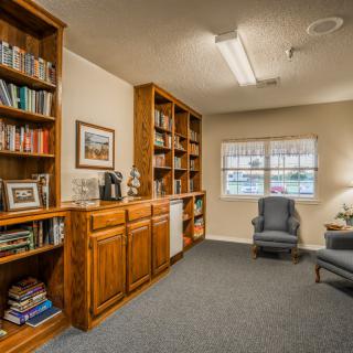 A cozy library room with wooden bookshelves, two armchairs, and a window.
