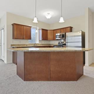 A modern kitchen featuring wooden cabinets, a central island, pendant lighting, and stainless steel appliances.
