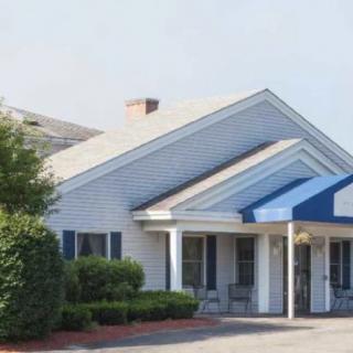 A building with a blue canopy over the entrance, surrounded by bushes.
