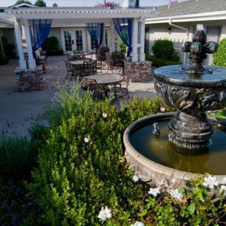 A serene garden patio with a central fountain, lush greenery, and comfortable outdoor seating.