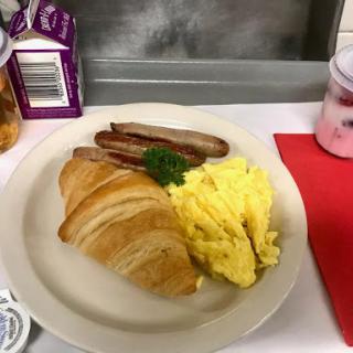 A delicious breakfast plate featuring scrambled eggs, a croissant, and sausage.