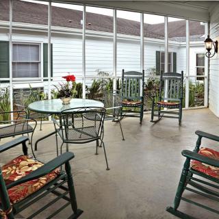 A cozy screened porch with rocking chairs and a glass table, adorned with potted flowers.