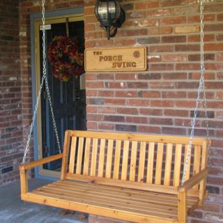 A cozy wooden swing on a porch, inviting relaxation in front of a brick wall.