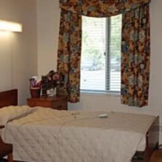 A simple room featuring a bed, nightstand, and window with floral curtains.