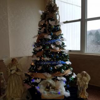 A beautifully decorated Christmas tree with ornaments, surrounded by angel figurines and a nativity scene.