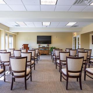 A well-lit conference room with arranged chairs facing a television and podium.