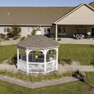 A picturesque gazebo on a well-manicured lawn in front of a residential house.
