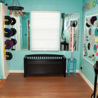 A colorful room with teal walls, featuring a collection of hats displayed on the walls, a large mirror, and a wooden floor.