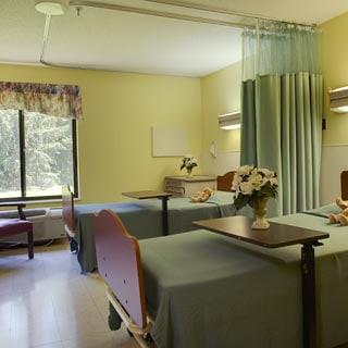A shared hospital room with two beds, a curtain divider, and a window view.