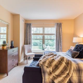 A cozy bedroom with a neatly made bed, dresser, and large window with curtains.