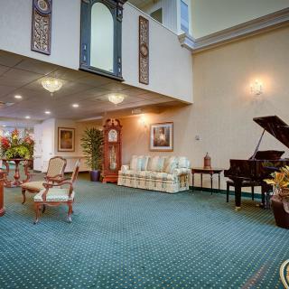 A spacious lobby area featuring a grand piano, elegant furniture, and decorative elements, illuminated by chandeliers.